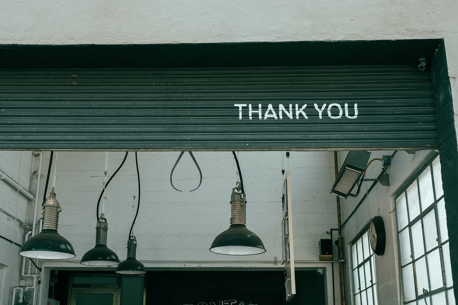 A roll-up door with “Thank you” painted on it, above hanging lamps